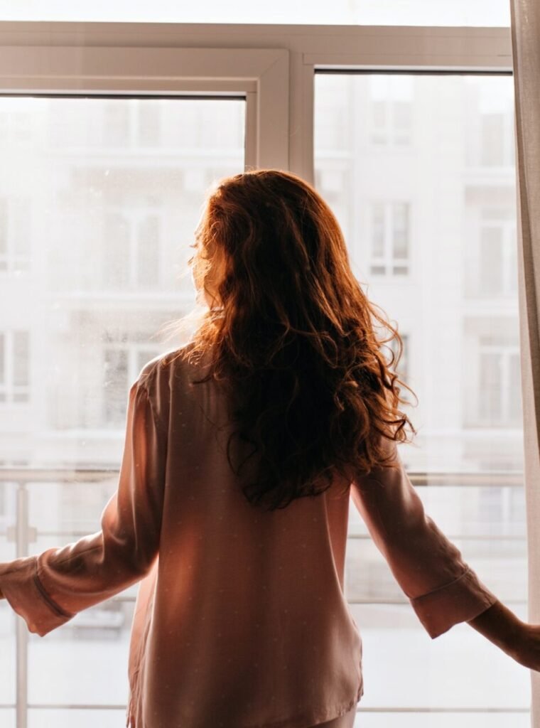 red haired girl touching curtains indoor photo of caucasian young lady standing near window